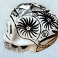 A decorative skull sculpture with intricate black sugar skull style patterns painted on an off-white base, set against a light blue textured background, right side view.