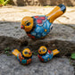 Three hand-painted ceramic bird figurines in yellow, decorated with intricate blue, black, red, green, and orange floral patterns, arranged on a rustic wooden surface top view.