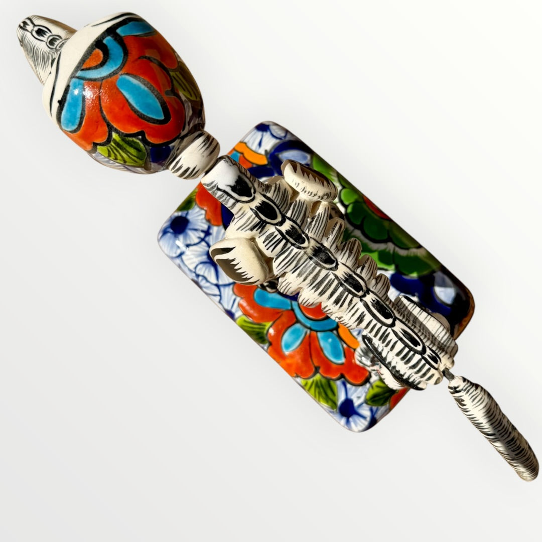 A ceramic Mexican-style skeleton dog figurine standing on a colorful floral base against a plain white background. Top view of catrina dog.