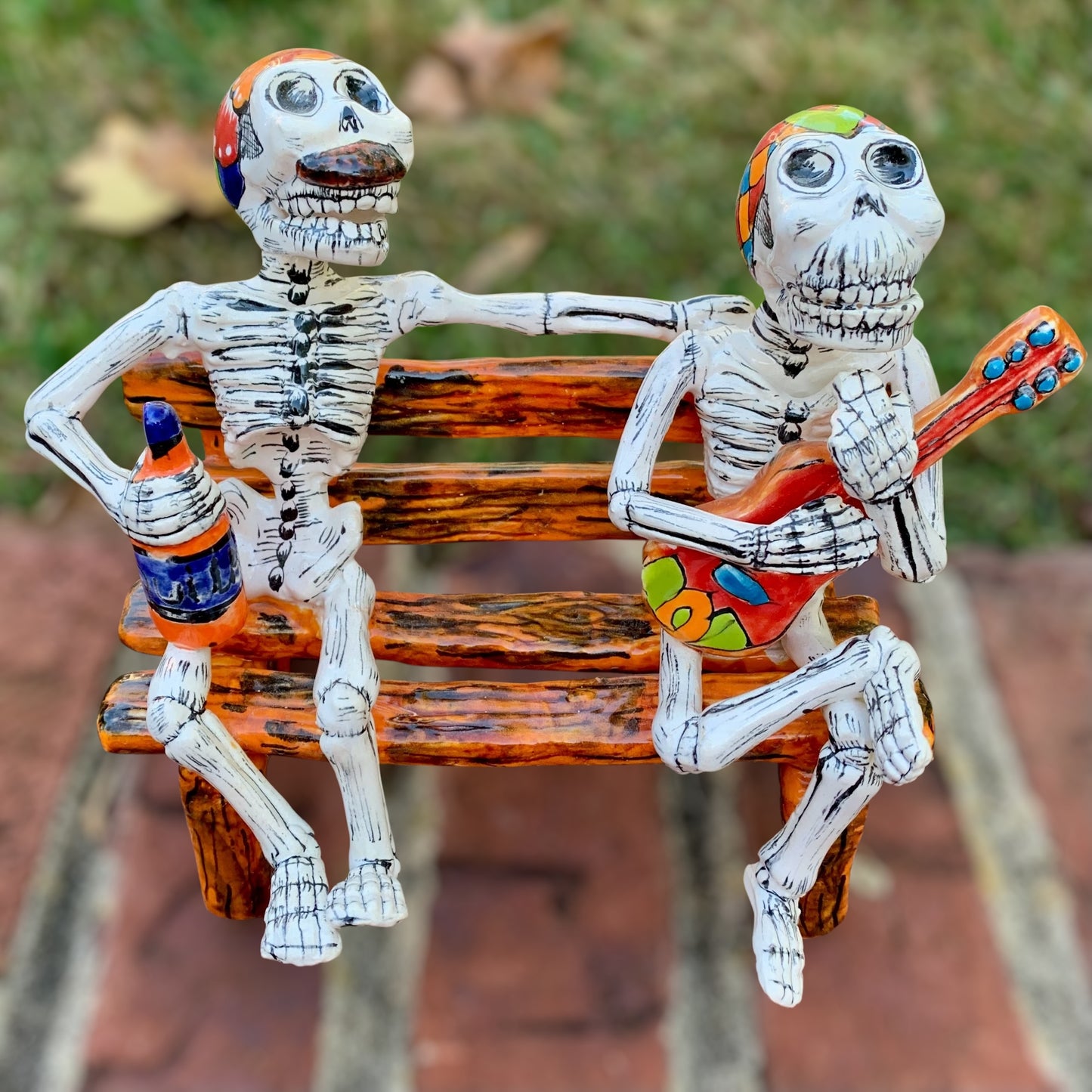 Two skeleton figurines sitting on a bench with one playing a guitar and the other holding a bottle.
