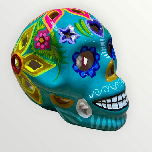 A decorative sugar skull painted in bright turquoise blue with colorful floral and geometric patterns in pink, yellow, green, purple, and white, shown against a plain light background.