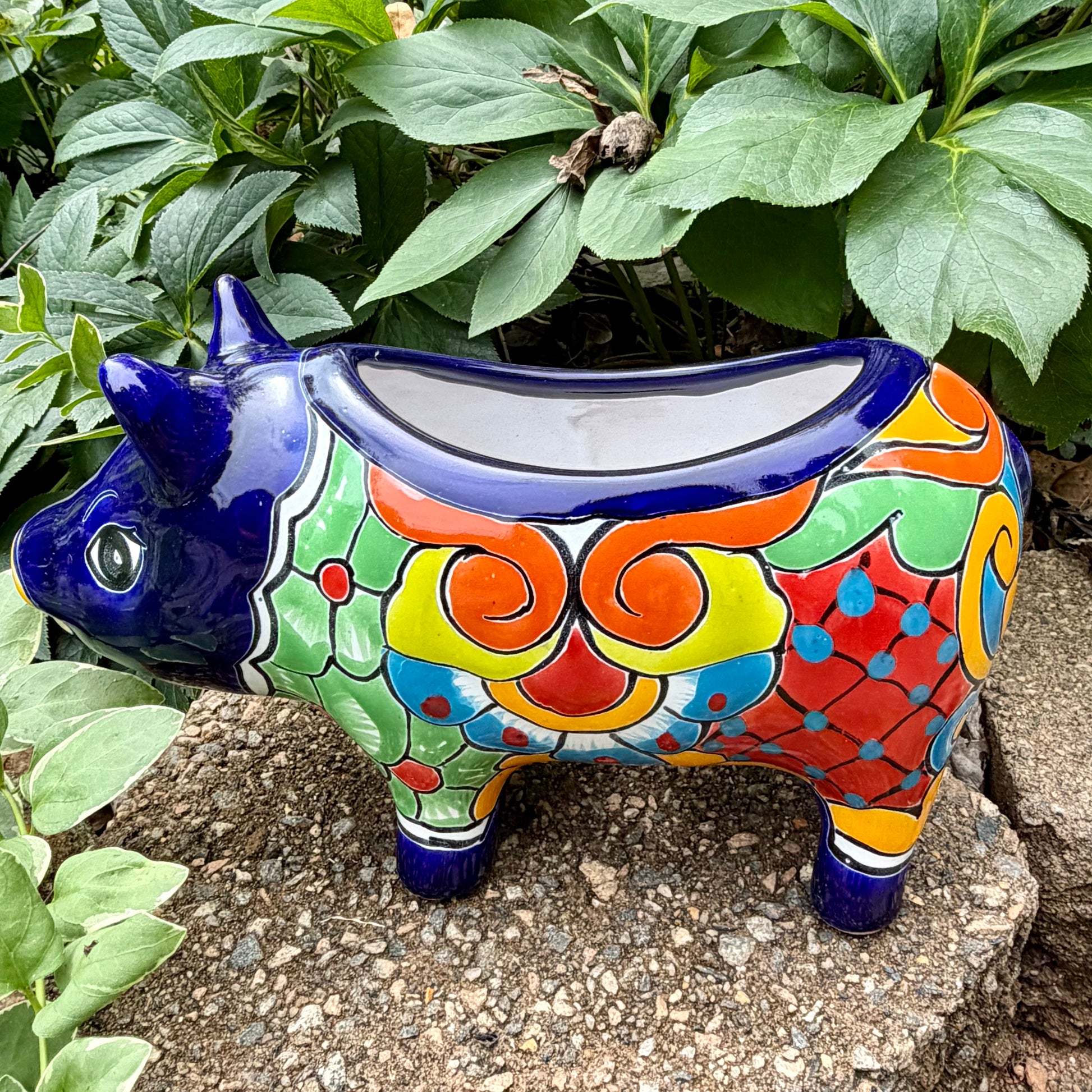 Colorful Talavera ceramic pig sculpture on a stone surface with green plants in the background Right side