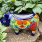 Colorful Talavera ceramic pig sculpture on a stone surface with green plants in the background Right side