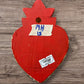 A Milagros heart featuring a gold textured top and a red heart base covered in raised silver-toned charms displayed on a wooden wall, back view.