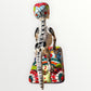 A ceramic Mexican-style skeleton dog figurine standing on a colorful floral base against a plain white background. Back view of catrina skeleton dog showing backbone
