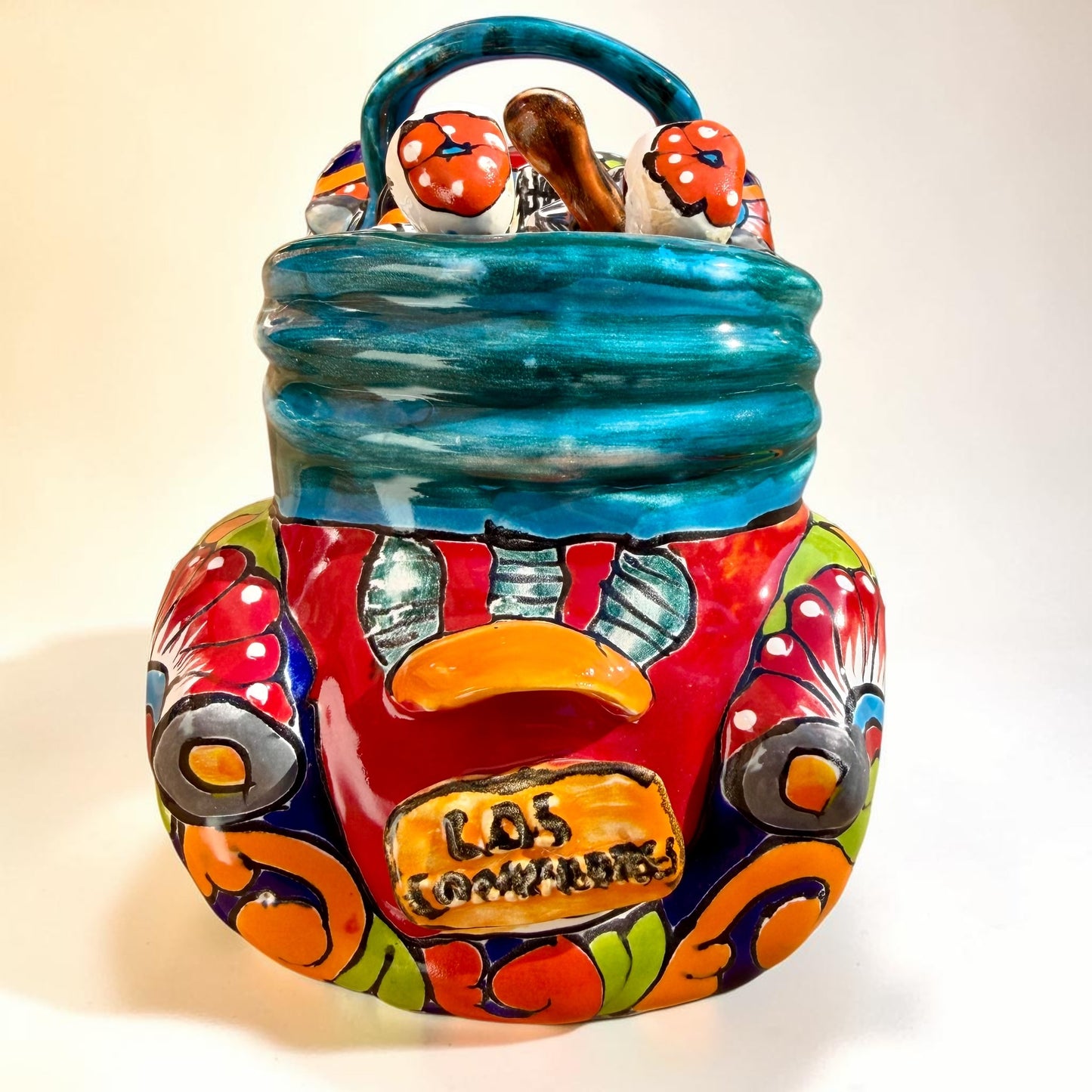 A colorful hand-painted ceramic Mexican-style convertible car figurine with Day of the Dead skeleton characters inside, shown on a neutral beige background. Back view of the care with license plate.