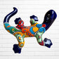 A colorful ceramic wall sculpture of a stylized lizard, decorated with vibrant hand-painted patterns in blue, orange, green, yellow, and red, mounted on a white brick wall back view