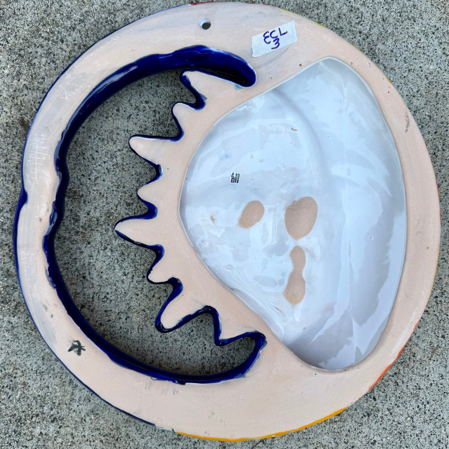 A colorful hand-painted ceramic wall plaque featuring a crescent moon and sun design, set against a gray stone background, back side view with hanging hole.