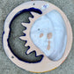 A colorful hand-painted ceramic wall plaque featuring a crescent moon and sun design, set against a gray stone background, back side view with hanging hole.