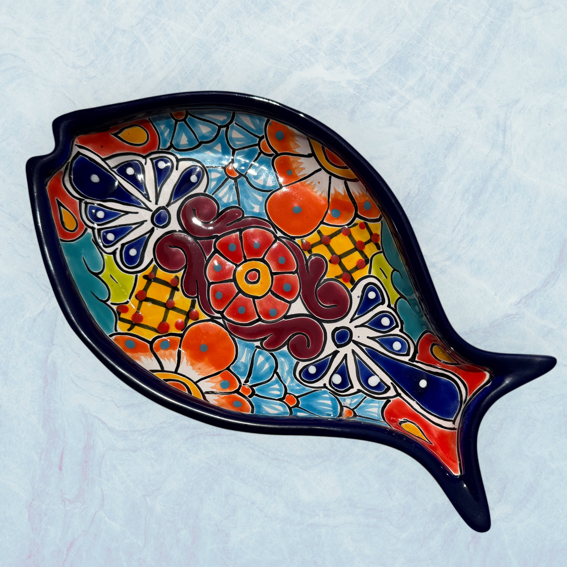 Blue decorative fish-shaped talavera serving plates with colorful hand-painted floral and geometric patterns, displayed on a light blue background.