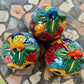 Three colorful hand-painted Talavera jack-o'-lantern pumpkins with multi-color displayed on a stone patio with a blurred green lawn background, top stem view.