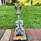 A colorful hand-painted Talavera Catrina donkey figurine, standing on a colorful floral base in an outdoor backyard setting, view of the back tail.