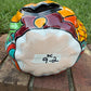 A Talavera jack-o'-lantern pumpkin decoration with a carved face, sitting on a brick surface in an outdoor yard with grass and trees in the background. Bottom of the pumpkin.