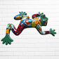 A colorful hand-painted ceramic frog wall sculpture in a dynamic jumping pose, decorated with vibrant green, red, orange, yellow, and blue patterns, set against a white brick wall background left side