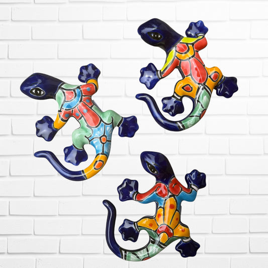 Three colorful ceramic gecko wall art pieces in a vibrant multicolor design, displayed against a white painted brick wall.