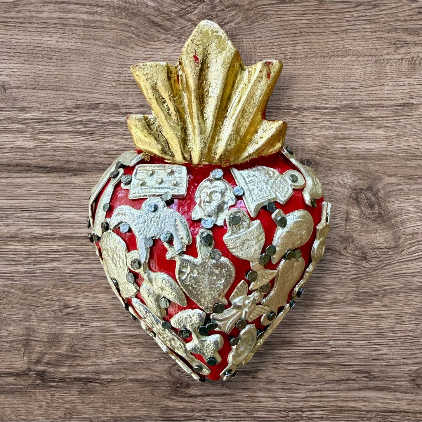 A Mexican Milagros heart in  red with a gold flaming top, covered in silver charms. 