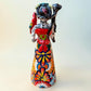 A Talavera Day of the Dead (Día de los Muertos) Frida figurine  with a monkey on her shoulder and a red parrot on her other shoulder, set against a light blue gradient background. Back view of figurine, showing monkey and parrot.