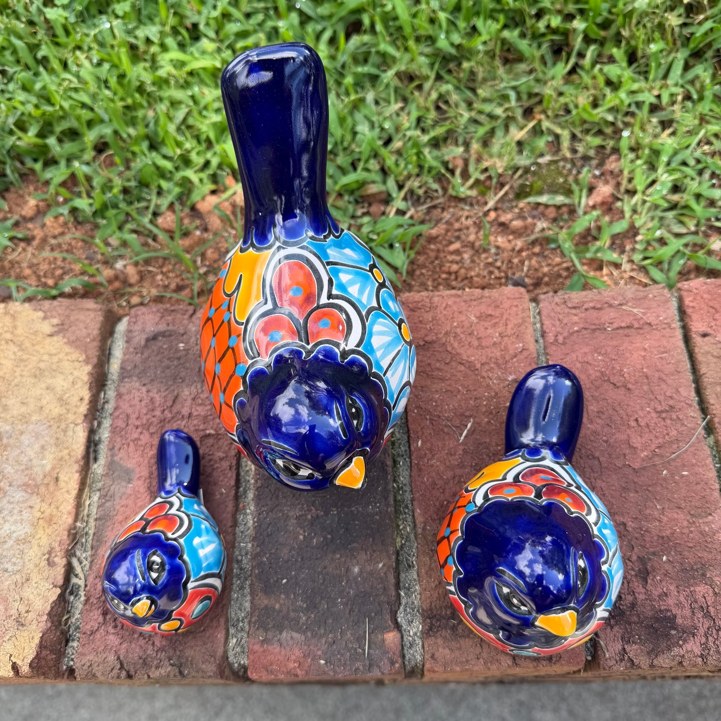 Three hand-painted ceramic bird figurines in different sizes, decorated with a vibrant Mexican Talavera style pattern of blue, red, yellow, and white, showing top view.
