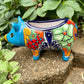 Colorful Talavera ceramic pig planter on a stone surface with green plants in  Background side view