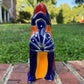 A colorful hand-painted Mexican Talavera Ceramic dog figurine sitting on a brick wall with a green grassy lawn and a house in the background front view.