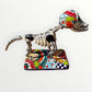 A ceramic Mexican-style skeleton dog figurine standing on a colorful floral base against a plain white background. Left side view of dog.