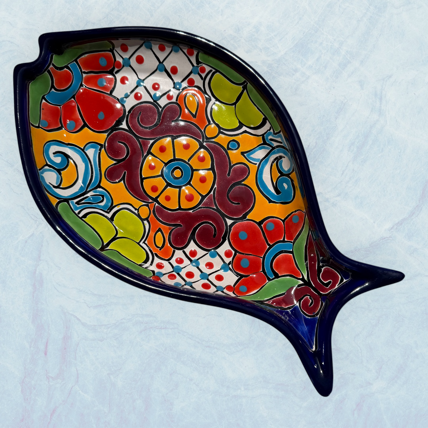 Blue decorative fish-shaped talavera dishes with colorful hand-painted floral patterns, displayed on a light blue textured background.