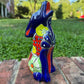 A colorful hand-painted talavera ceramic coyote figurine sitting on a brick surface with a blurred green lawn and trees in the background.