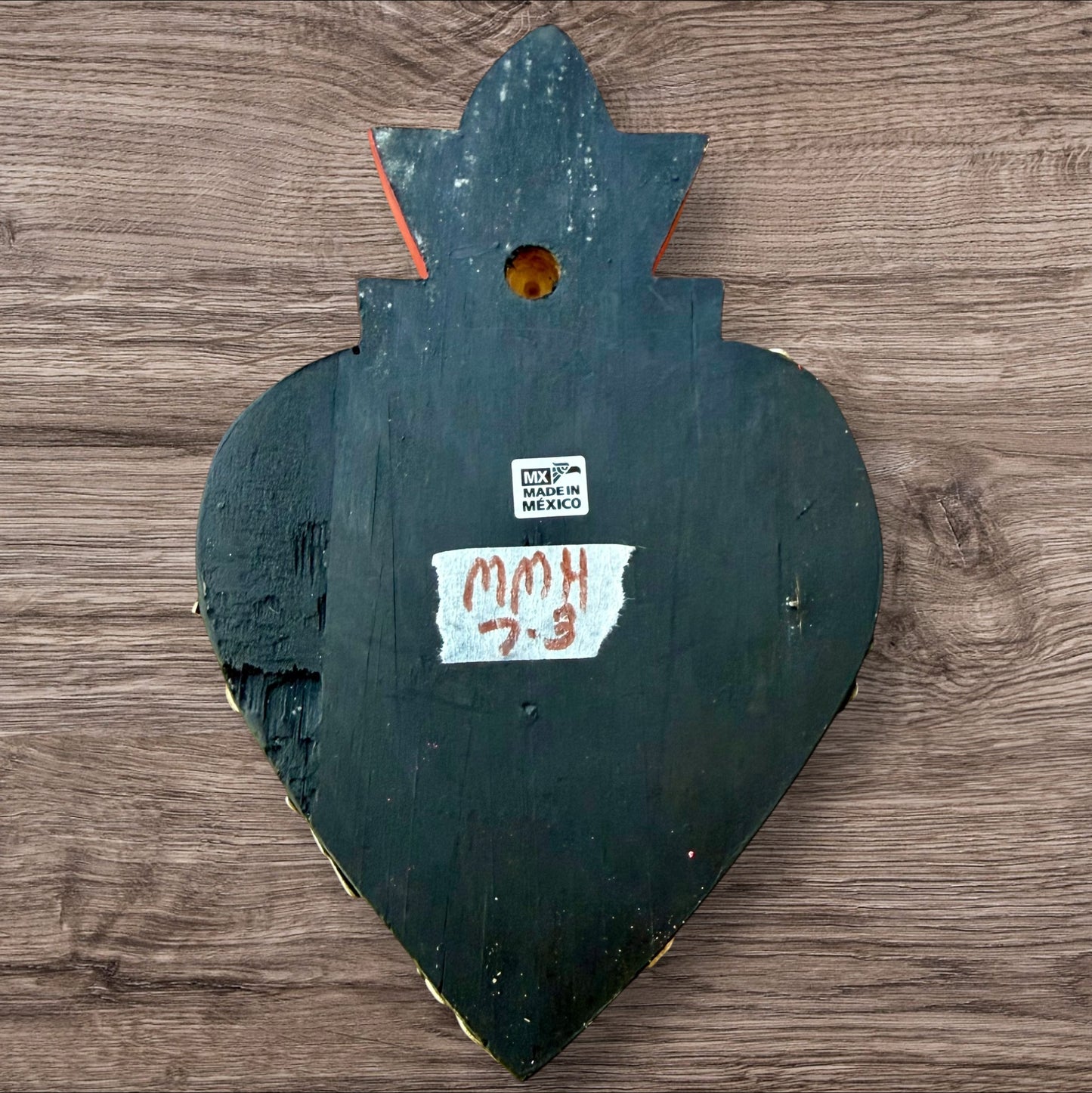 A Mexican Milagros medium heart in black with a gold and red flaming top, covered in antiqued golden charms, view of the back.