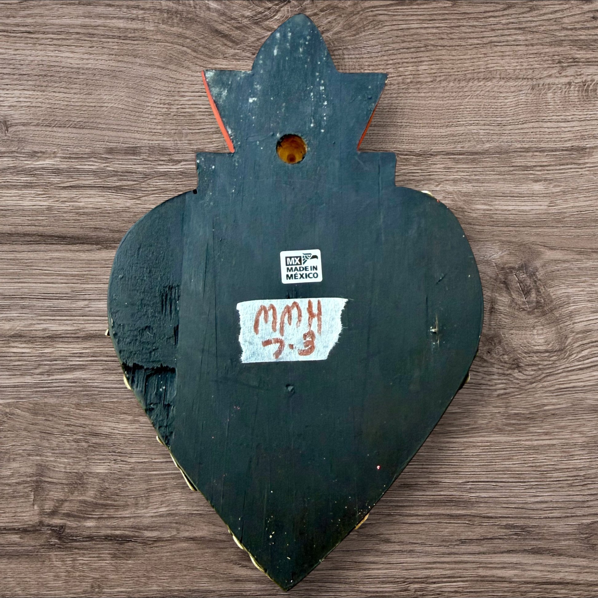 A Mexican Milagros medium heart in black with a gold and red flaming top, covered in antiqued golden charms, view of the back.