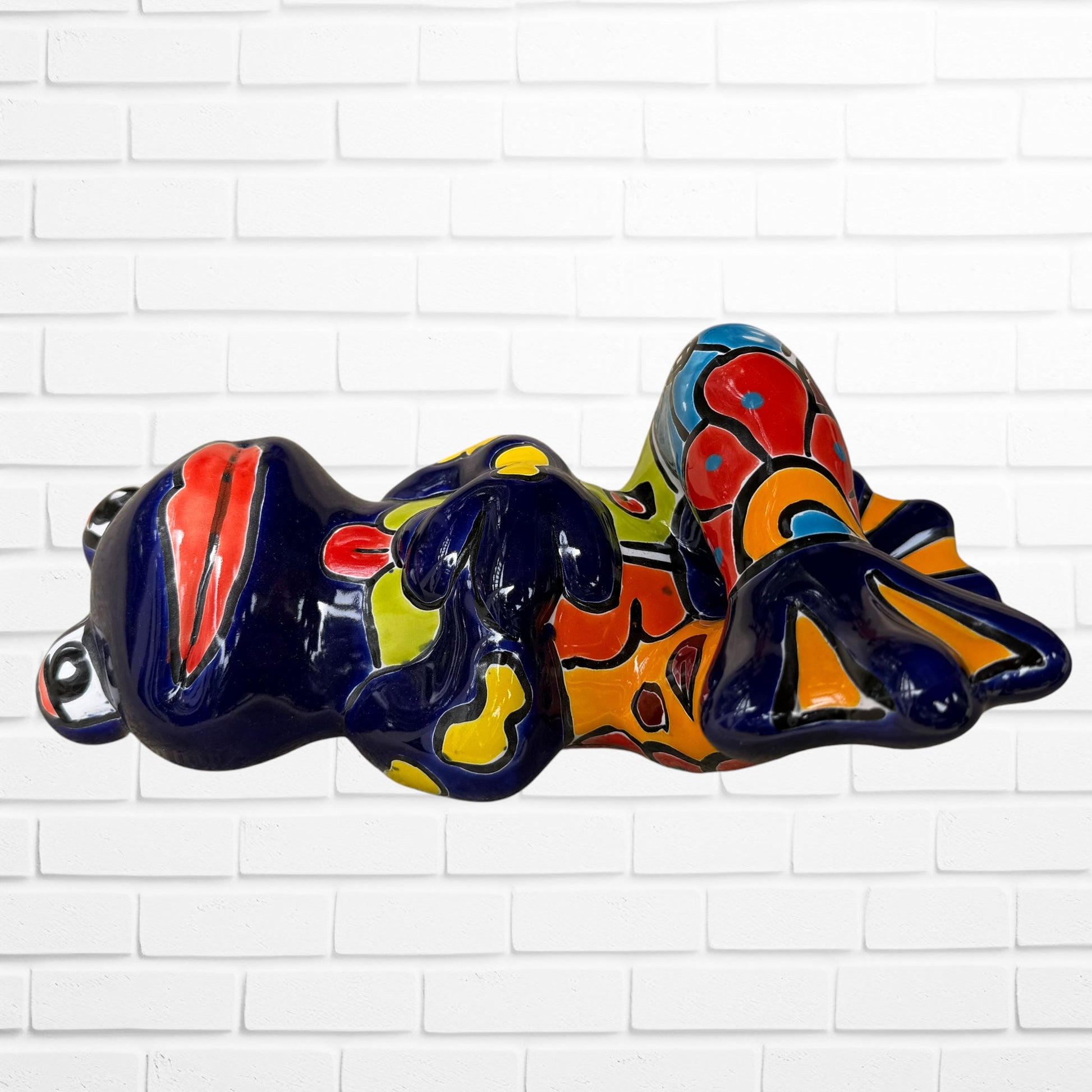A colorful ceramic frog figurine sitting with arms crossed, decorated with vibrant hand-painted patterns in blue, yellow, red, orange, and light blue, set Right side view.
