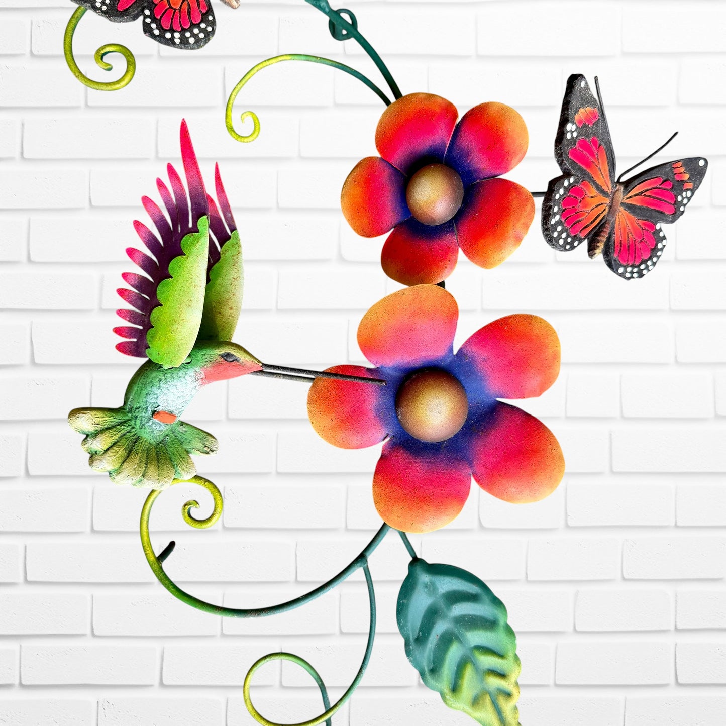 Decorative wall art with colorful flowers, a hummingbird, and butterflies on a white brick background center