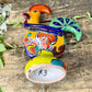 A colorful hand-painted ceramic Mexican-style rooster figurine standing on a rustic wooden surface outdoors, rooster bottom sculpture view.