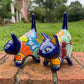 Two colorful hand-painted talavera ceramic cat figurines in cobalt blue with multi color designs standing on a brick path with a green lawn right side view.
