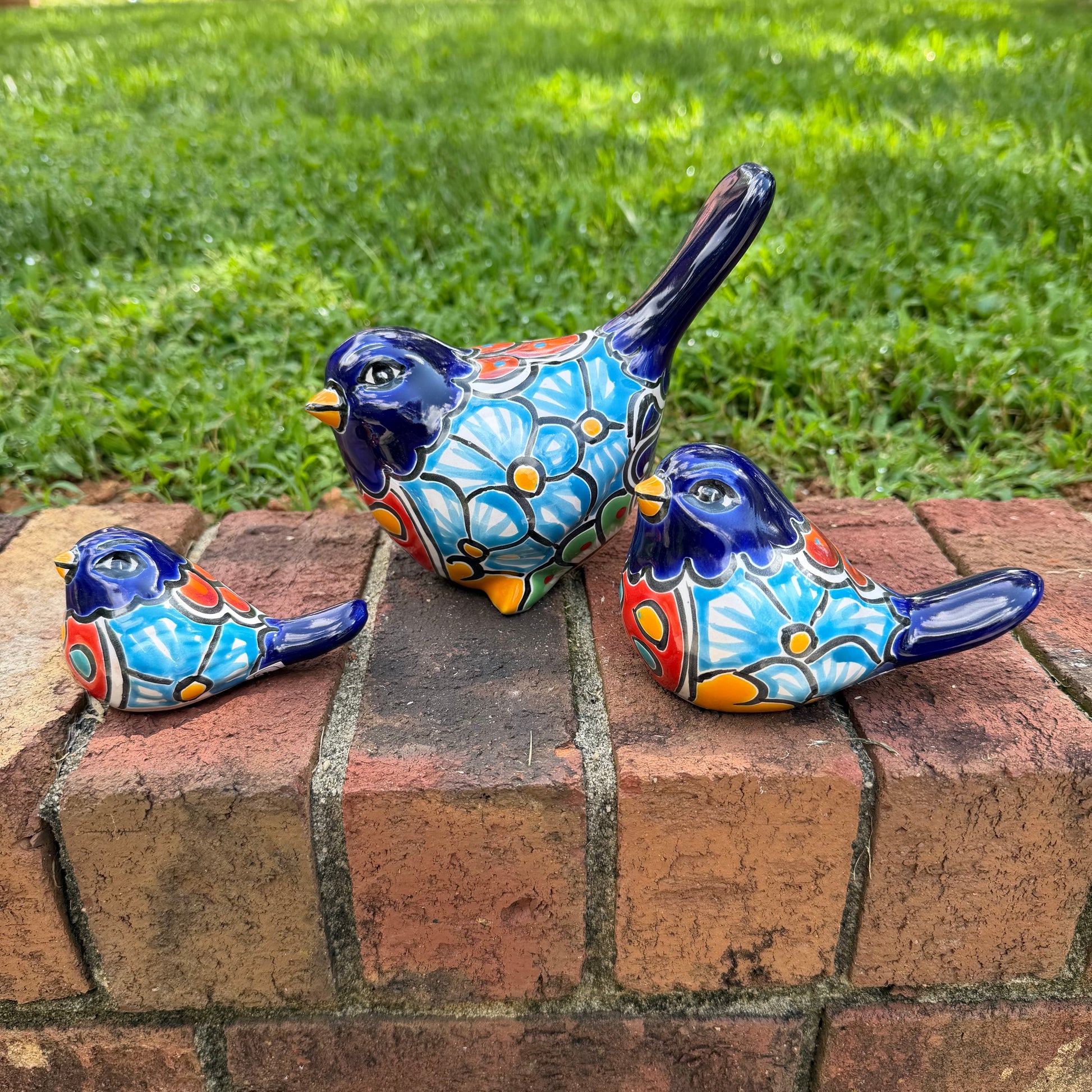 Three hand-painted ceramic bird figurines in different sizes, decorated with a vibrant Mexican Talavera style pattern of blue, red, yellow, and white, showing right side view.