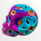 A hand-painted ceramic sugar skull in vibrant purple, turquoise blue, and yellow, decorated with floral and geometric patterns on a plain white background right side view.