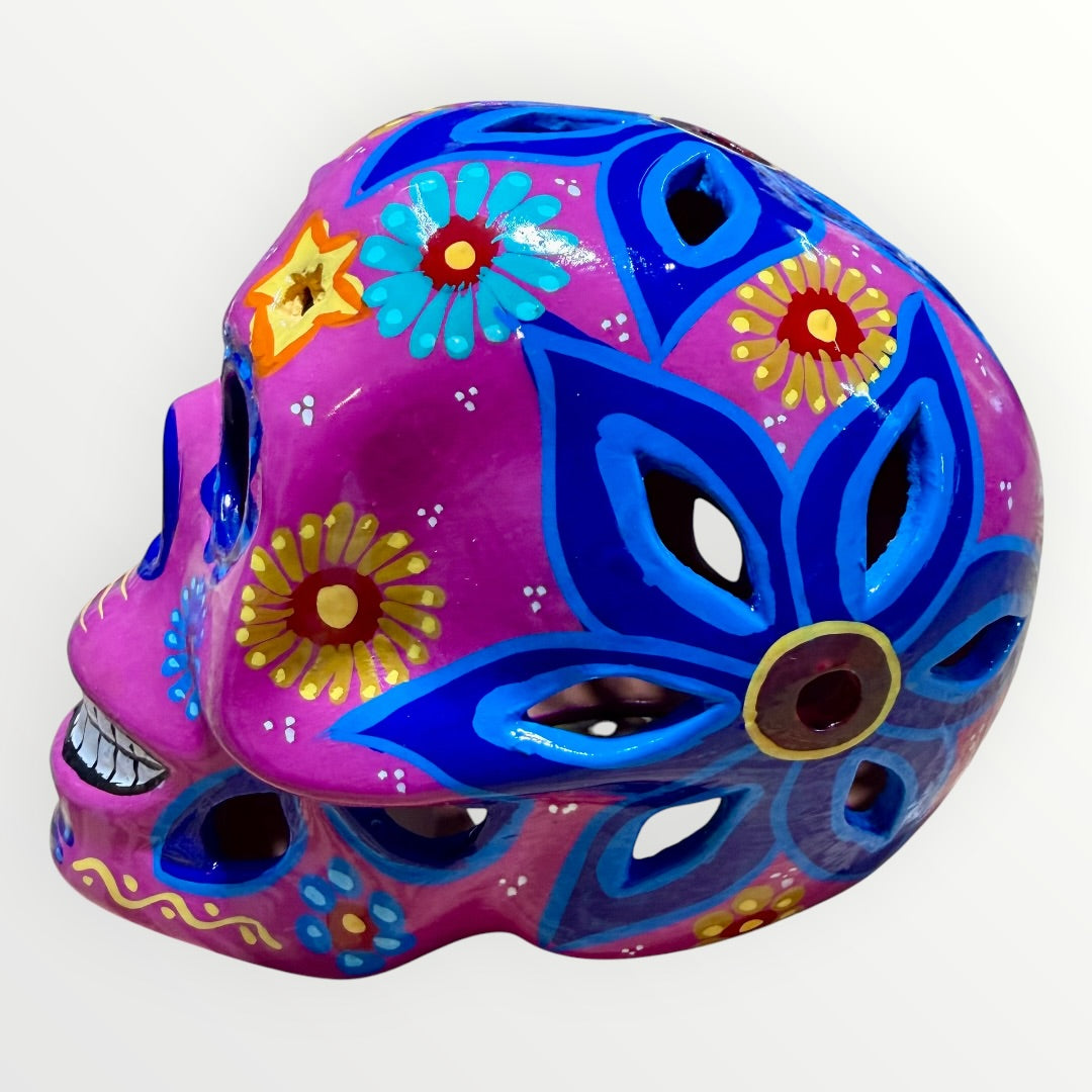 A hand-painted ceramic sugar skull mask in vibrant magenta pink, decorated with colorful floral and geometric patterns in blue, yellow, red, and white, set against a plain white background right side view.