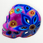 A hand-painted ceramic sugar skull mask in vibrant magenta pink, decorated with colorful floral and geometric patterns in blue, yellow, red, and white, set against a plain white background right side view.