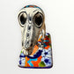 A ceramic Mexican-style skeleton dog figurine standing on a colorful floral base against a plain white background. Front view of dog showing face.