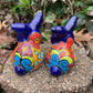 Two colorful Mexican Talavera rabbit figurines on a stone surface with greenery in the background set of two back view