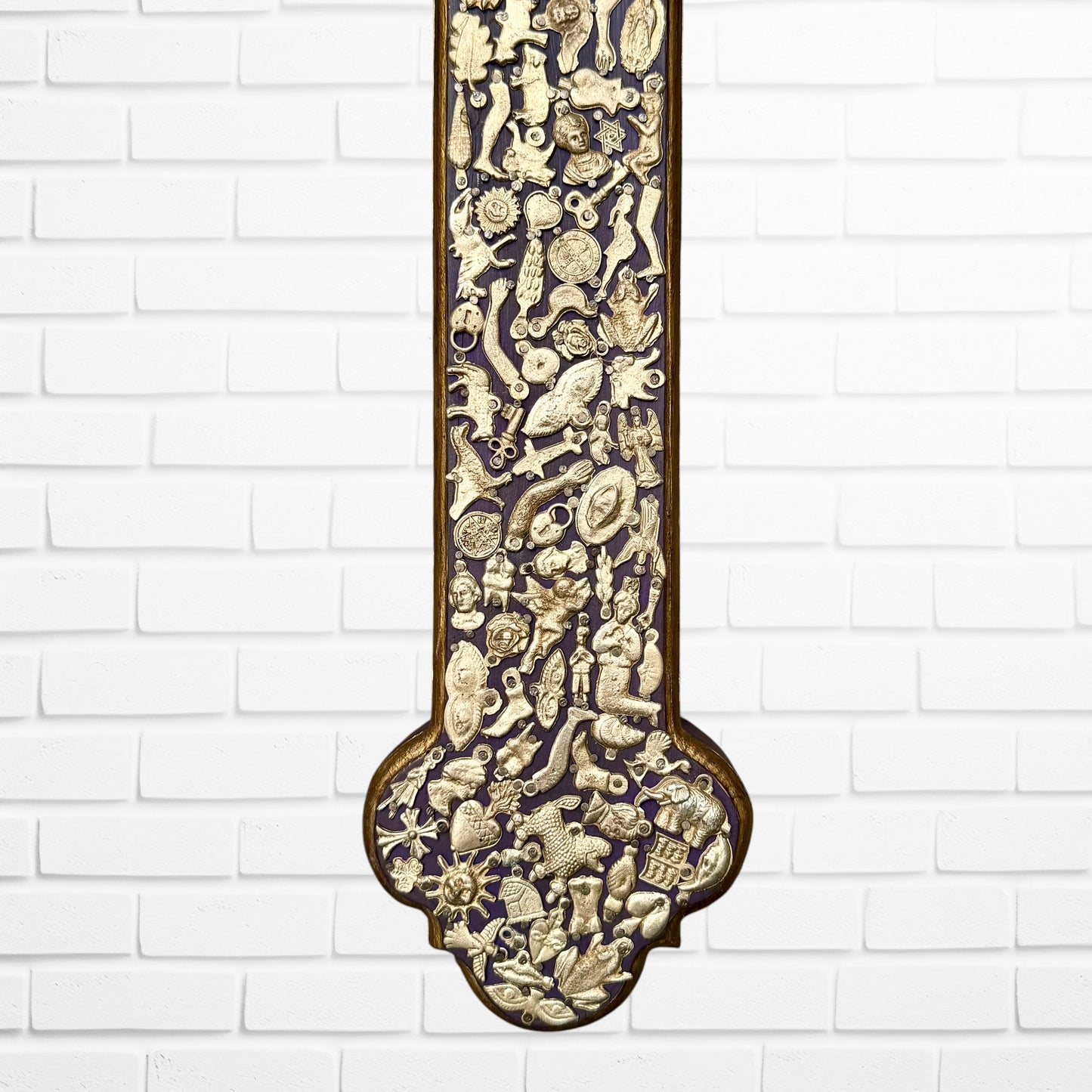 Decorative Milagros wood cross with many charms “miracles” on a white brick wall background Bottom half