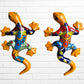 Two colorful hand-painted ceramic gecko wall sculptures in a vibrant Mexican folk art style, displayed side-by-side against a white brick wall.