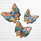 Three colorful ceramic Talavera butterfly wall art pieces with orange, blue, green, yellow, and purple mosaic patterns, displayed against a white brick wall.