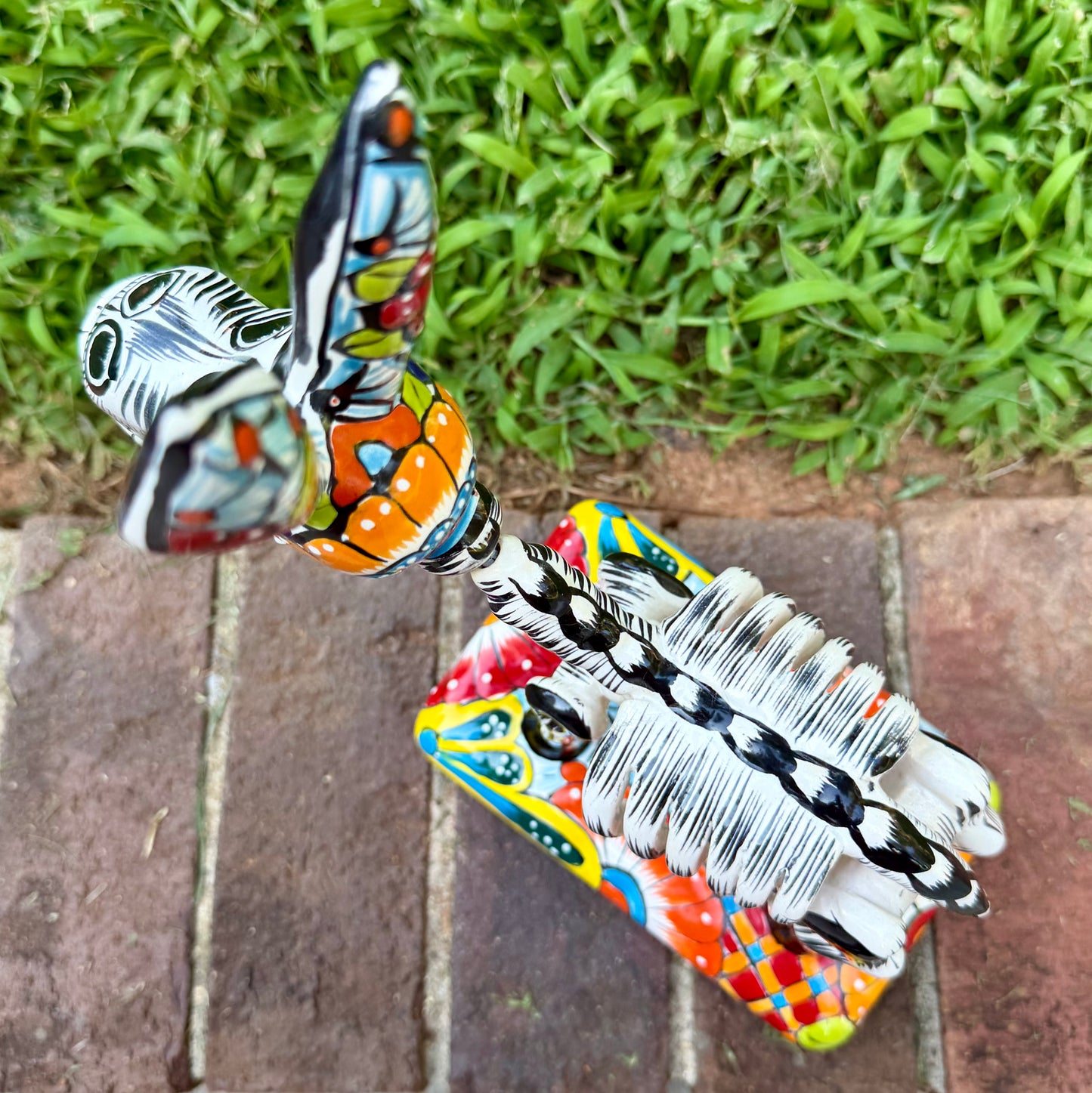 A colorful hand-painted Talavera Catrina donkey figurine, standing on a colorful floral base in an outdoor backyard setting, top view showing backbone.