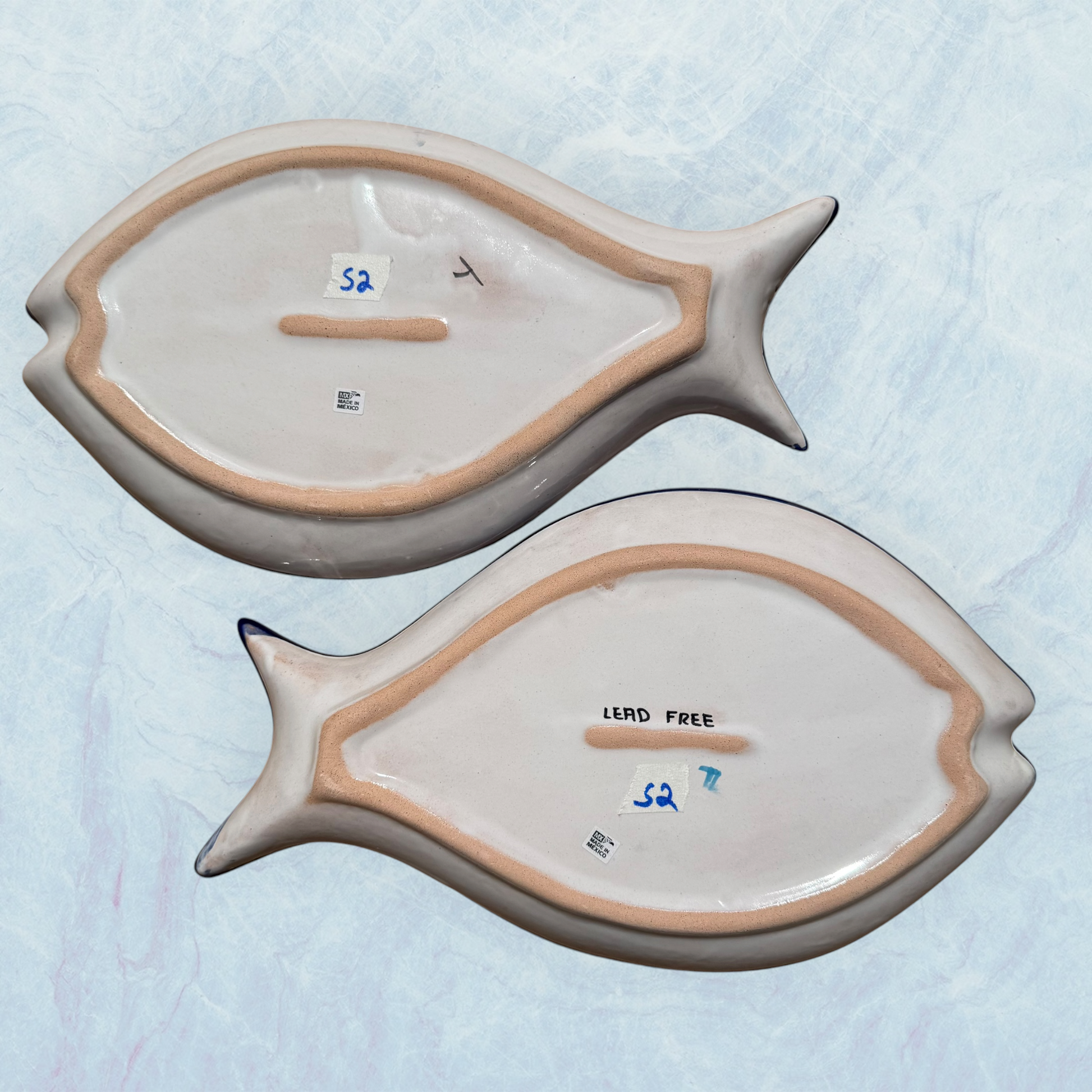 Two blue decorative fish-shaped talavera dishes with colorful hand-painted floral patterns, displayed on a light blue textured background back view of plates,