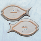 Two blue decorative fish-shaped talavera dishes with colorful hand-painted floral patterns, displayed on a light blue textured background back view of plates,