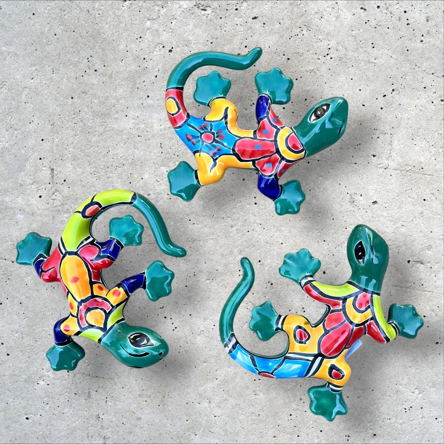 Three colorful Talavera ceramic lizards on a textured surface
