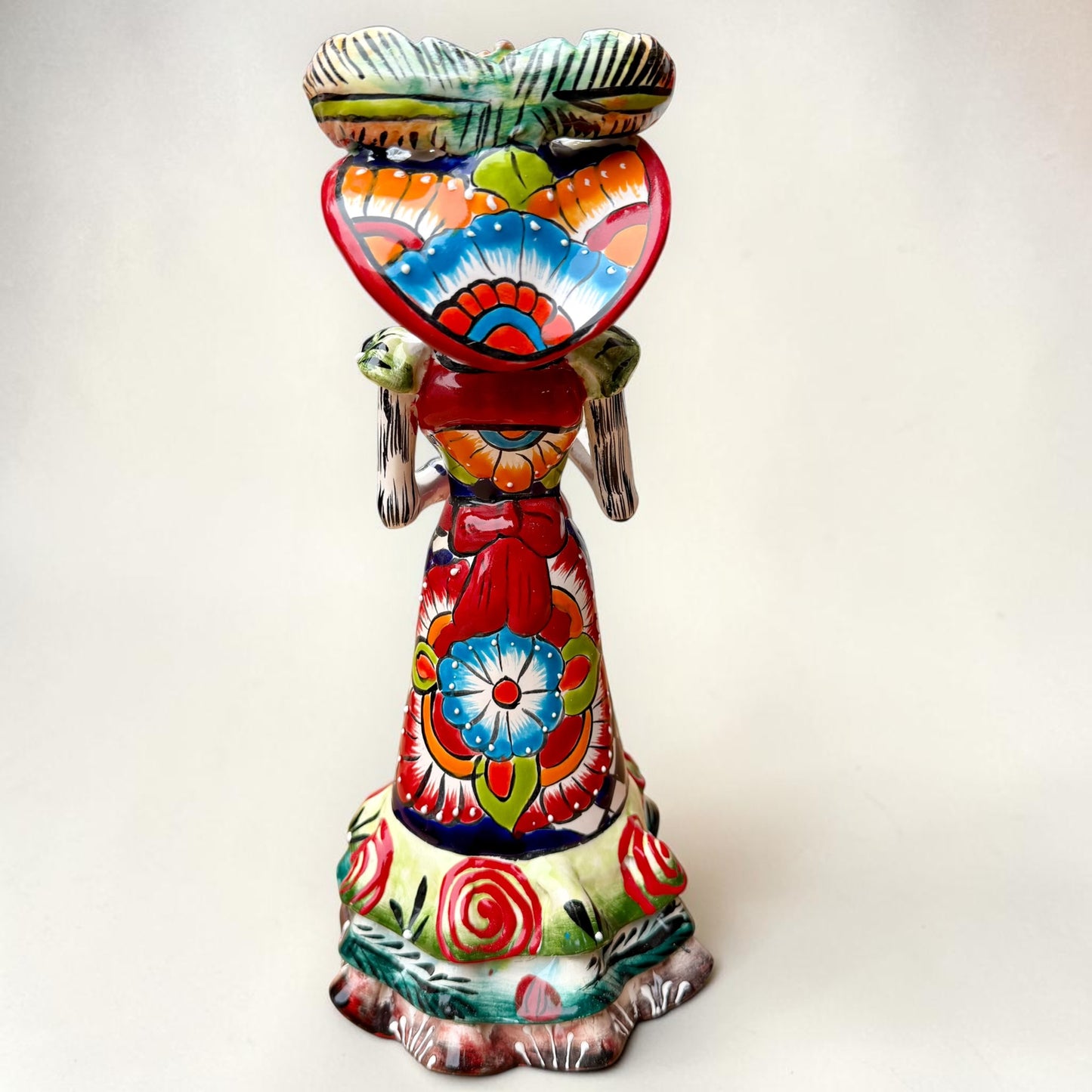 A colorful hand-painted talavera Day of the Dead (Día de los Muertos) skeleton figurine wearing a wide-brimmed sombrero and a floral dress, set against a plain off-white background. Back view of the doll.