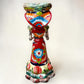 A colorful hand-painted talavera Day of the Dead (Día de los Muertos) skeleton figurine wearing a wide-brimmed sombrero and a floral dress, set against a plain off-white background. Back view of the doll.
