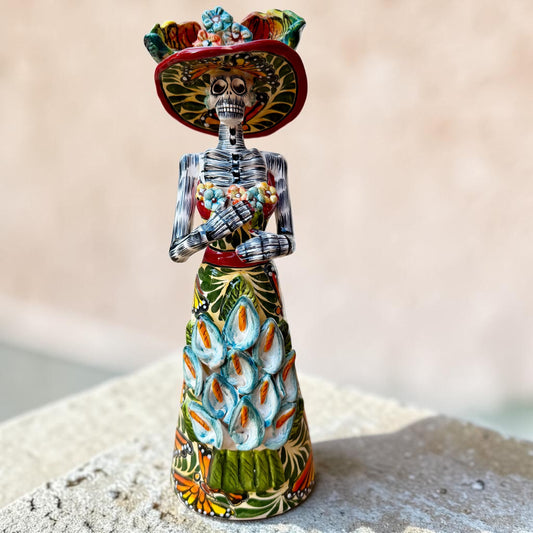 Mexican catrina talavera doll with calla lilies on the front of her dress. wearing a colorful dress with a big feathered hat.  