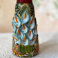 Mexican catrina talavera doll with calla lilies on the front of her dress. wearing a colorful dress with a big feathered hat.  Right side view of catrina. Close up of Calla lilies adorning the front of her dress.